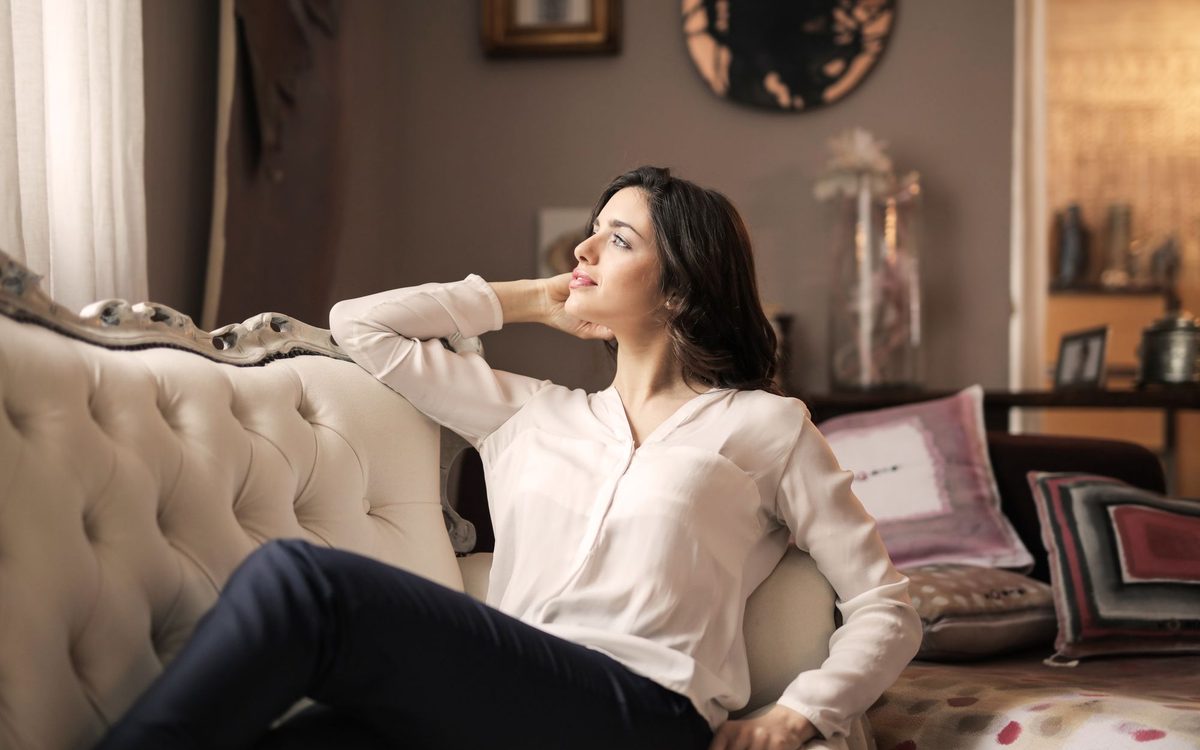 A serene woman enjoys a moment of reflection on a luxurious vintage sofa in a well-designed interior.