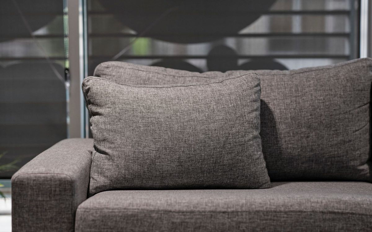 Close view of a grey woven-fabric sofa with a loose back cushion and wide arm