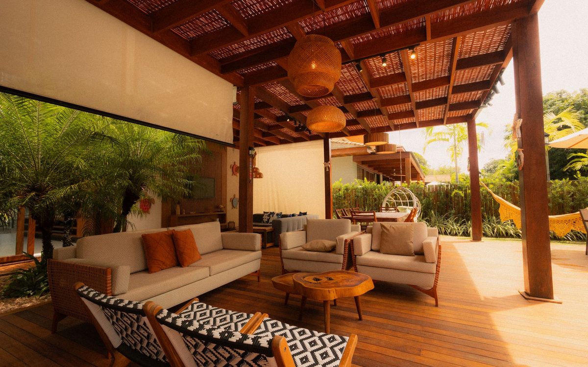 Covered outdoor living area with a cushioned sofa, lounge chairs, a live-edge wood coffee table and woven pendant lamps